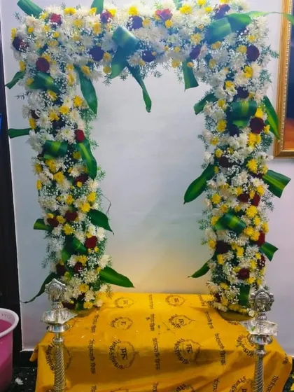 A beautiful floral arch setup for a Varamahalakshmi pooja at home. The two silver lamps on either side complete the divine setup.