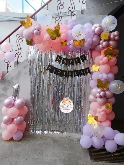 A pastel pink and purple butterfly-themed balloon arch with a silver shimmer curtain.