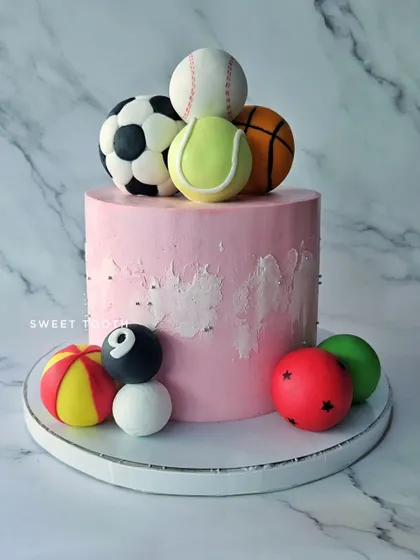 A cake with all her favorite toys. This pink black forest cake is decorated with a variety of edible sports balls, from football to tennis.