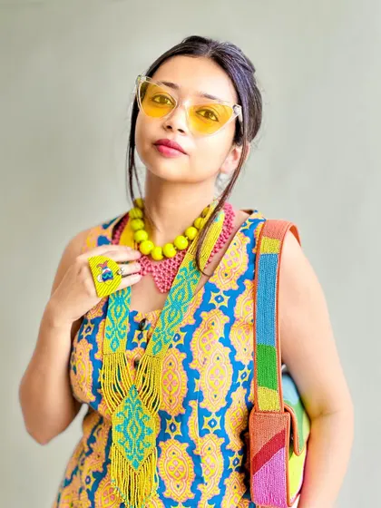 A portrait shot showing the layered necklaces and colorful bag. The yellow-tinted glasses add to the Y2K, hippie aesthetic.