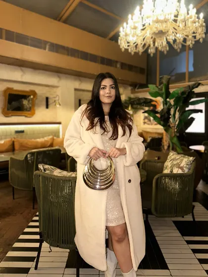 A glamorous evening look. A sequined mini dress layered under a cozy cream-colored teddy coat, accessorized with a statement metallic clutch.