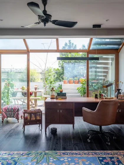 The study in the Dhaka home, a space designed for focus and inspiration, looks out onto the garden through floor-to-ceiling glass walls. The dark wood flooring and leather office chair create a classic, sophisticated feel, while the view provides a constant connection to nature.