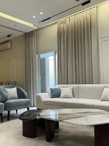 This living room features a combination of a large sofa and two matching accent chairs in a soft blue fabric. The nesting marble coffee tables add a layer of sophistication and practicality to the space.