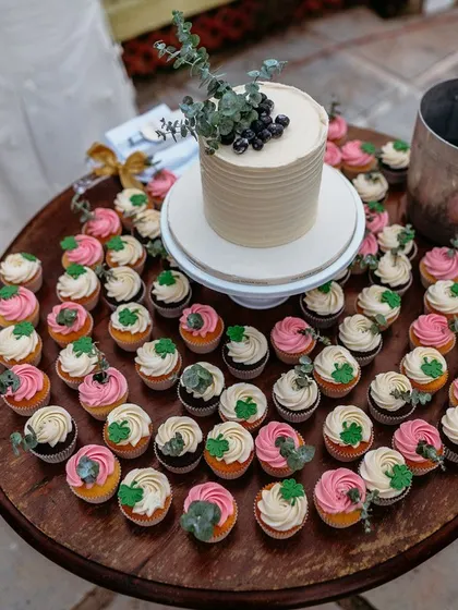 A table full of delicious cupcakes surrounding a small wedding cake, offering guests a variety of sweet treats to enjoy.