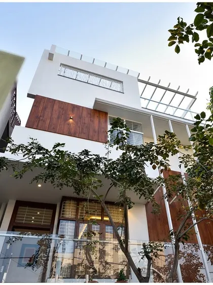 An upward view of Mr. Ramu Siddappa's residence, showcasing the clean lines of the balconies and the interplay between solid white walls and wooden accents.