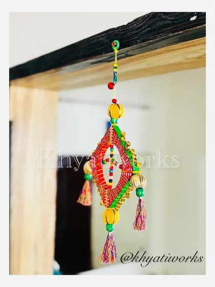 Another angle of the kite hanging. The wooden frame is wrapped in colorful thread and decorated with hand-painted details, making each one a unique piece.