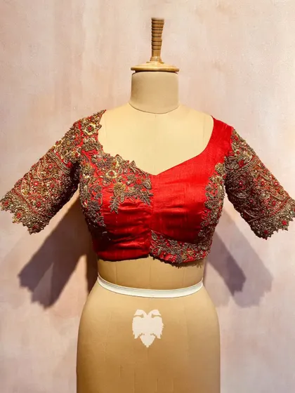 A frontal view of the red raw silk blouse with the wedding procession motif, showing the detailed floral embroidery on the sleeves.