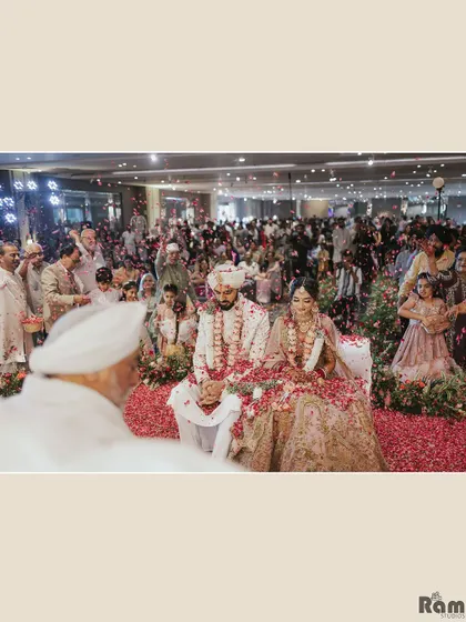 A beautiful wide shot of the wedding ceremony, with the couple seated at the mandap, showered with rose petals by their guests.