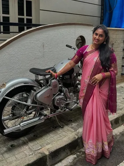 Our client looking lovely in a pink pure Mysore crepe saree with Bentex embroidery, posing next to a classic motorcycle.