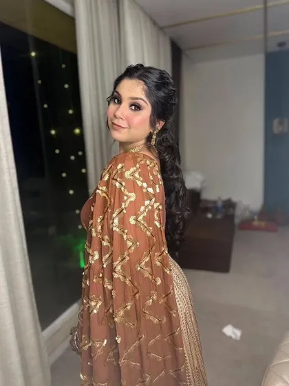 A playful glance over the shoulder. This hairstyle features a stylish curly ponytail, perfect for dancing the night away at a Sangeet.