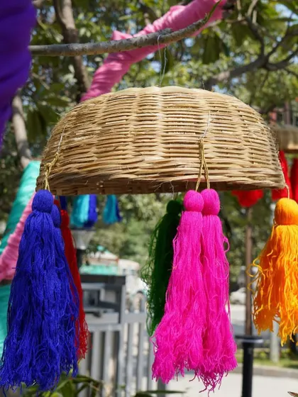 A close-up of a hanging basket with colorful tassels. These rustic and bohemian elements are perfect for adding a unique, handcrafted feel to an outdoor Mehendi or Sangeet.