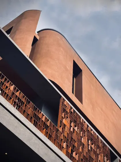 A detail shot focusing on materiality and rhythm. The terracotta tiling and bronze-detailed balcony railings create a tactile contrast against the building's sharp, modernist lines, showcasing a dialogue between texture and geometry.