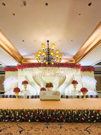We specialize in creating opulent reception stages that serve as the magnificent centerpiece of your celebration. This design features a grand floral canopy of red and white roses with cascading crystal elements.