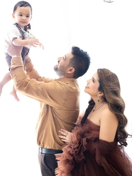 A father joyfully lifts his baby boy into the air as mom looks on with love. This high-key, bright photo style creates a dreamy and ethereal feel.