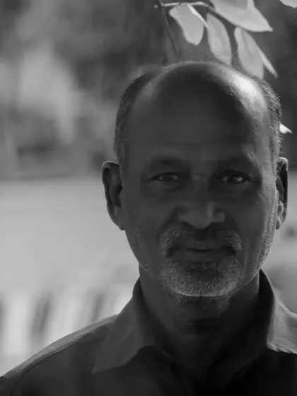 A black and white portrait of a man looking directly into the lens. The natural light and simple background keep the focus entirely on his expression.