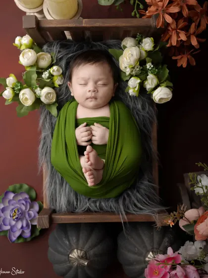 The simple elegance of a green swaddle against a dark background makes this newborn's peaceful sleep the central focus. The surrounding props add a touch of rustic charm.