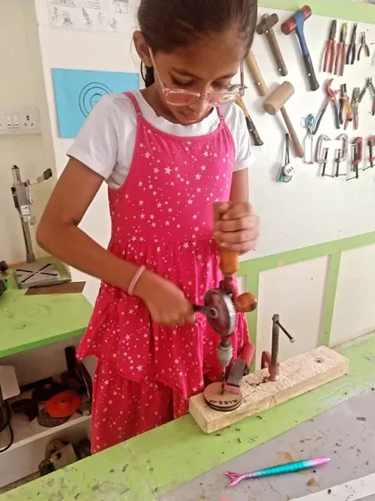 This young creator is hard at work with a hand drill, showing great concentration. Our tool wall in the background displays the variety of equipment we use.