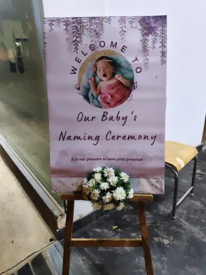 Another welcome board for a naming ceremony, with a simple easel and a small bouquet of white flowers.