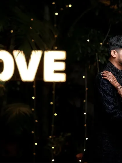 A romantic night shot of a couple standing by a "LOVE" marquee sign, perfect for an evening reception.