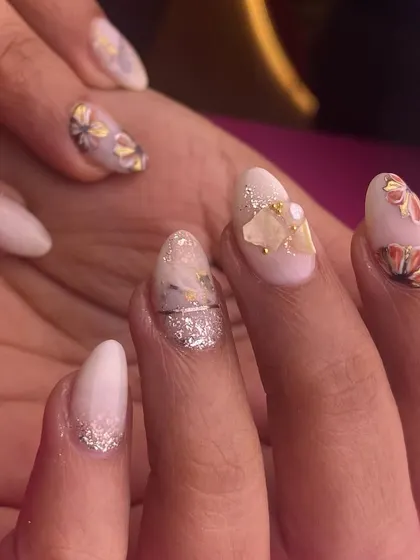 A soft and romantic nail set perfect for a bride or bridesmaid. The design includes a mix of glitter, subtle marble effects, and 3D floral details on a light, natural base.