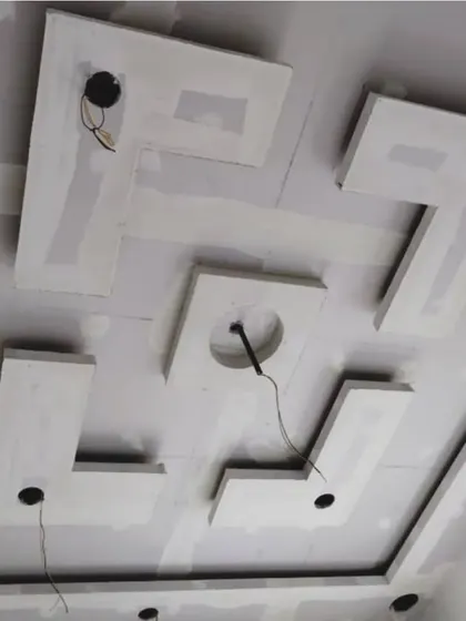 This image shows the structural build of a multi-layered geometric ceiling design. Each piece is precisely cut and installed to create a sharp, modern look before the POP finishing is applied.