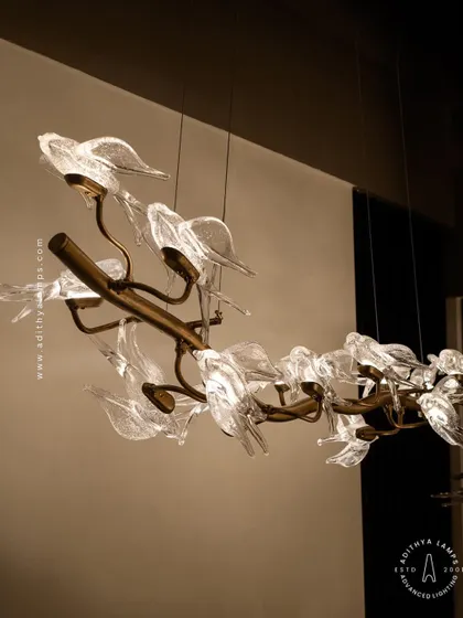 This horizontal chandelier features a flock of glass birds perched on a branch, as if in mid-flight. It's a perfect statement piece for suspension over a long dining table or in a living room, adding a dynamic and natural element.