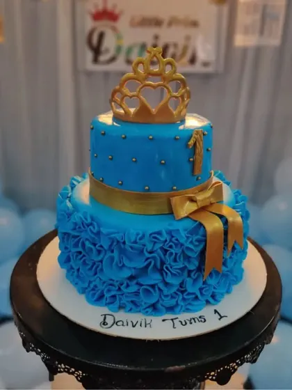 A royal blue two-tiered prince cake with a golden crown and ruffle details. It's a handsome and regal choice for your little prince's first birthday.