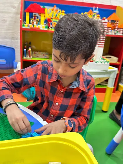 A young boy carefully assembles a LEGO landscape, demonstrating fine motor skills and concentration.