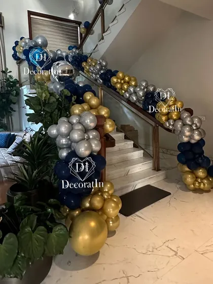A balloon garland in blue, silver, and gold elegantly drapes down a staircase, leading guests to the party.