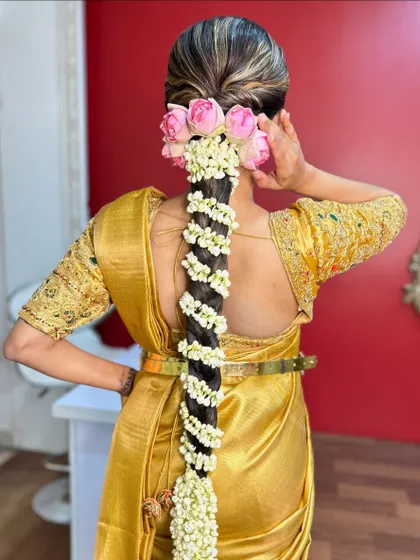 A full view of the traditional braid with pink roses and jasmine, showcasing the beautiful color combination against the gold saree.