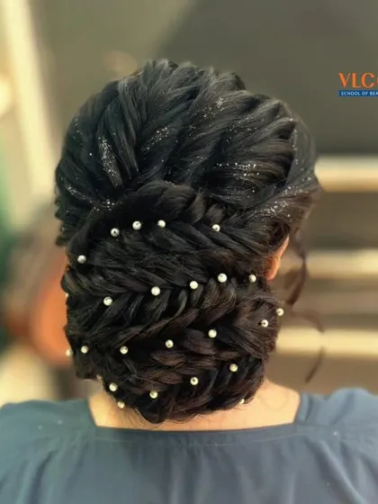 An elegant bridal updo featuring interwoven braids, sparkling glitter, and delicate pearl pins. This hairstyle is perfect for a reception or engagement ceremony.