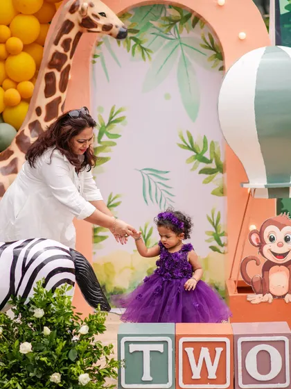 The birthday girl, dressed in a beautiful purple gown, stands out against the jungle backdrop. The 'TWO' blocks are perfectly sized for little ones to interact with.