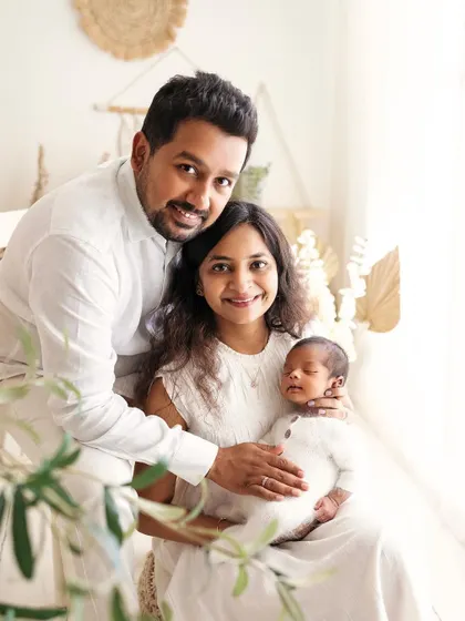 A beautiful family portrait with their newborn baby. The all-white outfits and boho decor create a bright, airy, and joyful image.