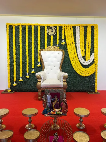 A greenery wall backdrop with a side draping of yellow marigolds. This asymmetrical design is modern and perfect for a Seemantham or Haldi ceremony.