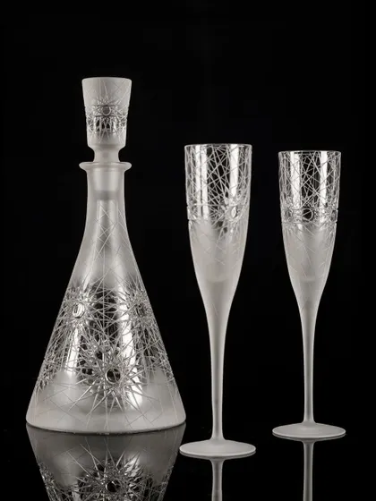 A frosted glass decanter and champagne flute set. The soft, diffused lighting enhances the delicate, etched patterns on the glassware.