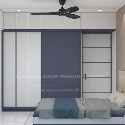 This bedroom showcases a sliding wardrobe with a dual-tone finish of white and deep blue. The design is modern and space-saving, complemented by a backlit circular mirror on the adjacent wall.