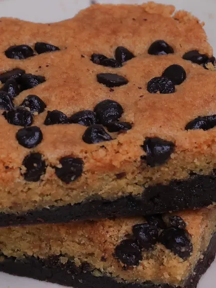 A close-up shot of our Cookie Dough Brownie, showing the contrast between the dark, fudgy brownie base and the golden, chip-studded cookie dough topping.
