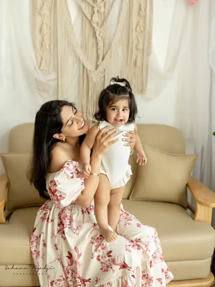 A mother holds her daughter on the sofa. The daughter's slightly shy but sweet expression is a lovely moment captured.