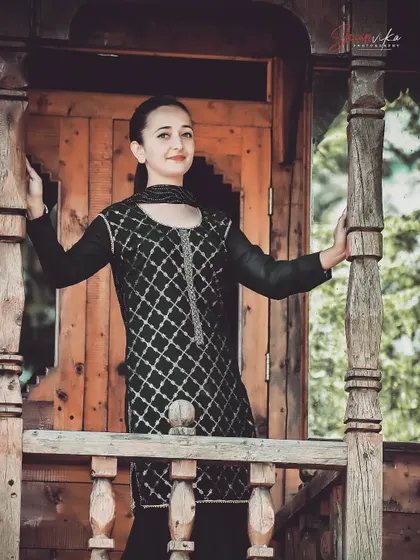 An elegant portrait of a woman in a traditional black suit, framed by a rustic wooden balcony. This setting adds a lot of character and texture to the image.