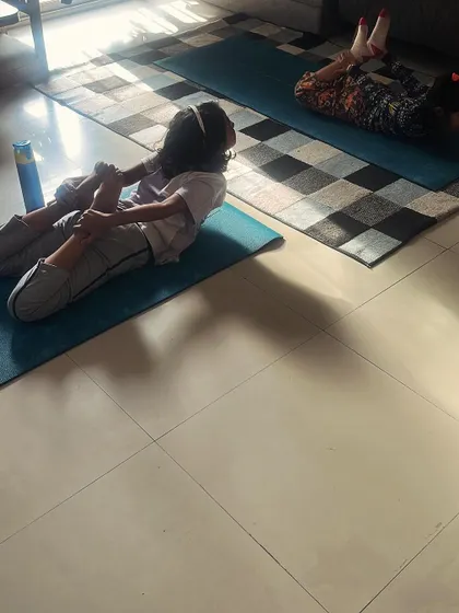 Two young girls practice a stretching pose together, showing the flexibility and body awareness that yoga develops.