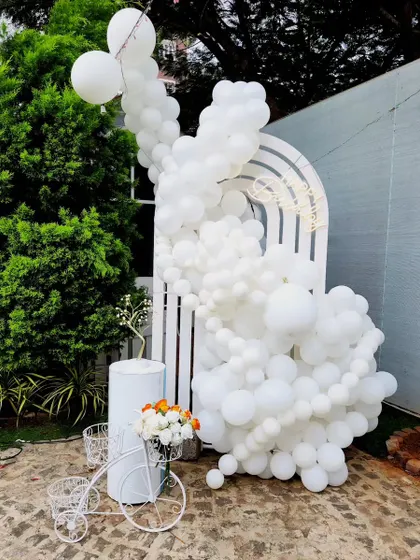 An all-white balloon arrangement with a matching arch backdrop and decorative bicycle creates a clean, elegant, and modern look.