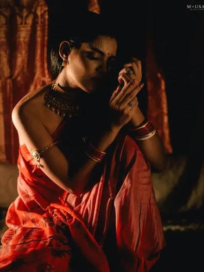 An editorial portrait of a model styled as a traditional Odia bride. The dark, moody lighting and her contemplative pose create a powerful, artistic, and soulful image.