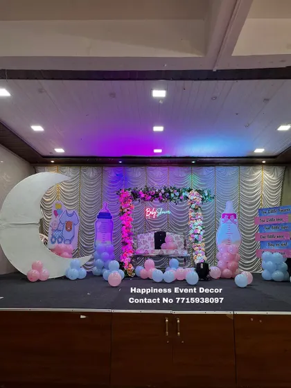 A simple yet beautiful baby shower stage setup. It includes a floral-decorated jhula, a large moon prop, and baby-themed cutouts like milk bottles, all highlighted with soft lighting.