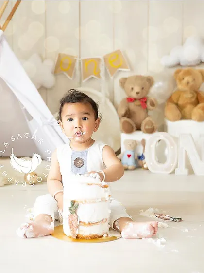 A classic cake smash moment. This little boy is enjoying his cake in a fun, whimsical tent-themed setup, complete with teddy bears and soft clouds.