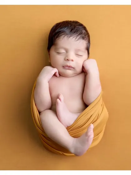 A perfect example of the classic "tucked-in" pose. Wrapped snugly in a mustard swaddle, this portrait highlights the baby's peaceful face and tiny feet.