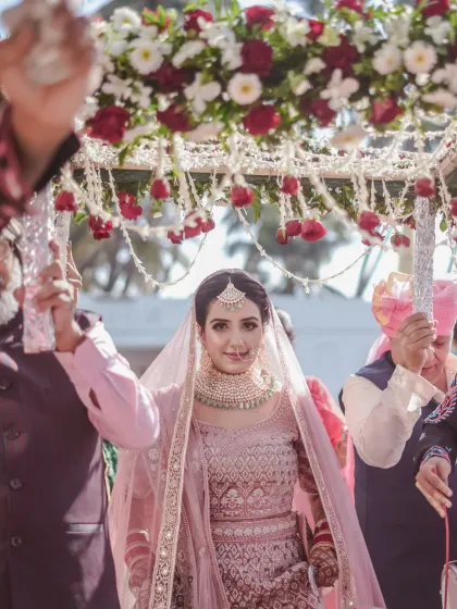 The bride's grand entrance under a beautiful 'phoolon ki chadar'. Her direct gaze at the camera captures her confidence and anticipation in this iconic wedding moment.