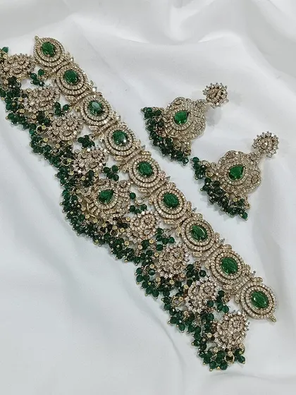 This choker set is available in multiple colors including ruby, emerald, and grey. The intricate metalwork combined with colored stones and pearl or bead droppings offers a sophisticated and royal look.