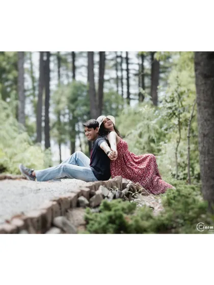 A sweet moment of connection, with the couple sitting back-to-back in a forest setting, holding hands. It's a simple yet powerful pose that symbolizes trust and partnership.