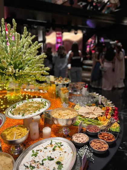 A vibrant and colorful grazing setup for a festive party, with a table covered in marigold petals. The spread includes various dips, chips, nuts, and other munchies, creating a lively and celebratory feel.