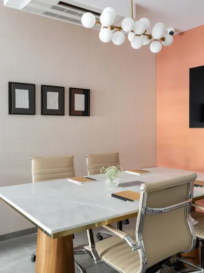 The conference room combines a marble-topped table with comfortable leather chairs and a modern bubble chandelier. The peach-colored accent wall adds a touch of warmth and personality to the space.